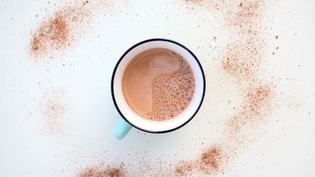 Top view of a steaming hot chocolate mug with cocoa sprinkles on a white surface.