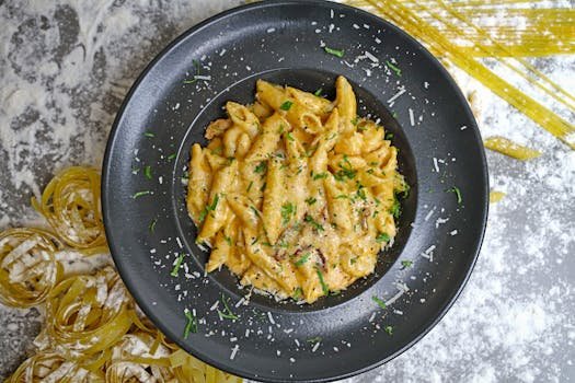 Top view of creamy penne pasta garnished with herbs and cheese, served on a dark plate.