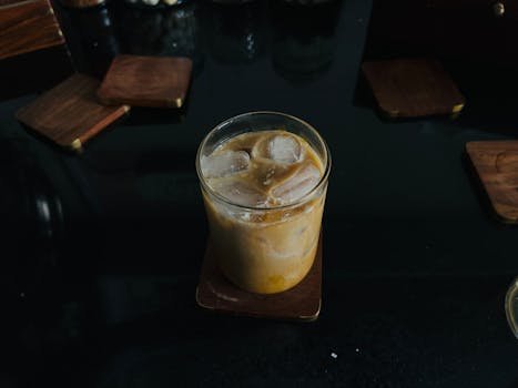 A glass of iced coffee on a wooden coaster, perfect for a refreshing break.