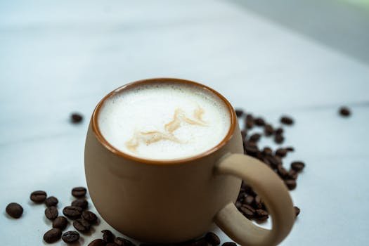 Close-up of a flat white coffee with latte art in a brown mug, surrounded by coffee beans.