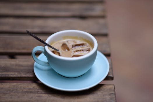 Iced coffee served in a blue cup on a rustic wooden table outdoors.