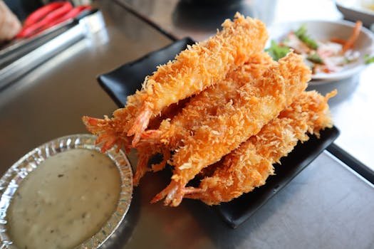 Golden fried shrimp served with creamy dipping sauce on a black platter.