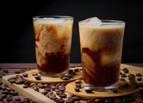 Delicious iced coffee with swirling cream served in glass cups surrounded by coffee beans.