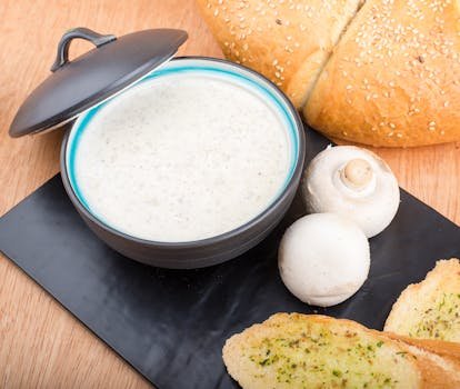 A delicious bowl of creamy mushroom soup served with fresh bread and garlic toast on a wooden surface.