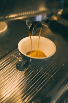 Rich espresso shot pouring from a machine into a gray ceramic cup. Perfect for coffee lovers.