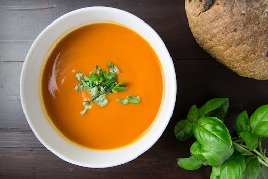 Delicious homemade tomato soup served with basil leaves and rustic bread.