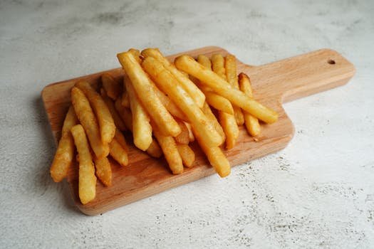 Golden, crispy French fries stacked on a wooden cutting board, ideal for food enthusiasts.