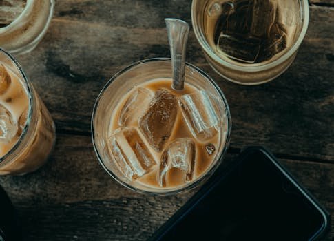 Overhead view of iced coffee with ice cubes in glass on rustic wooden table, perfect for refreshing break.